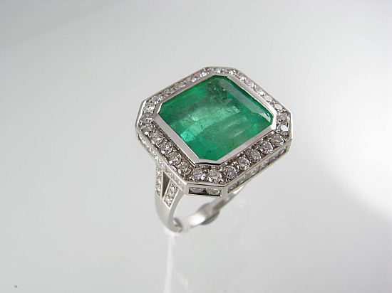 Lot 174. AN EMERALD AND DIAMOND SQUARE CLUSTER RING bezel-set in 18ct white gold.<br>Est $10000-11000