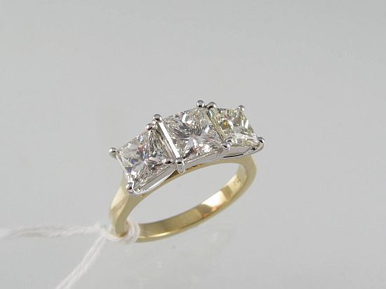 Lot 239. A THREE STONE PRINCESS-CUT DIAMOND RING claw-set in 18ct gold. <br>Est $8500-9000